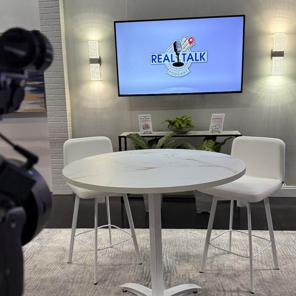studio with white table and two chairs Real Talk Logo on TV screen behind the table